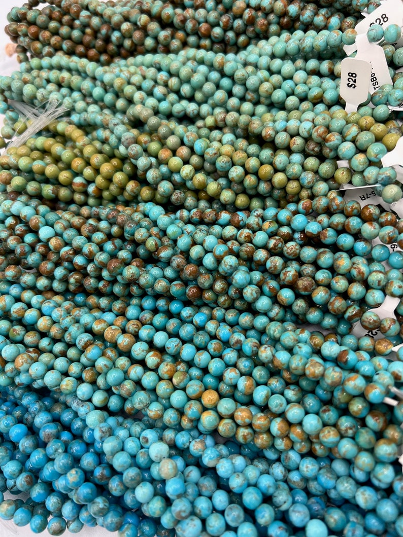 May include: A close-up of a strand of turquoise beads. The beads are a mix of blue and green with brown speckles. The beads are round and smooth. The price tag reads $28.