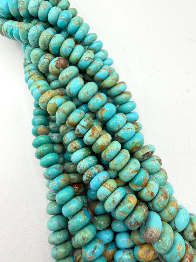 May include: A strand of round, disc-shaped turquoise beads featuring a vibrant sky-blue color with natural brown matrix veining throughout. The beads are arranged in a dense, vertical cluster, showcasing their smooth, polished surfaces and consistent size.