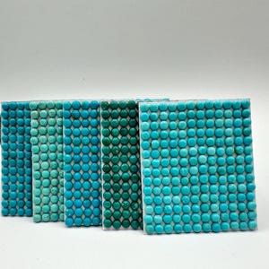 May include: A collection of rectangular tiles, each covered in small, round, turquoise-colored stones. The tiles vary in shades of blue and green, creating a gradient effect. The stones are evenly spaced, giving a textured appearance.