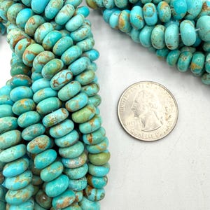 May include: A strand of round, disc-shaped turquoise beads featuring natural brown matrix veining in shades of bright blue and green. A United States quarter coin is placed next to the beads to provide a clear sense of scale for the bead size.