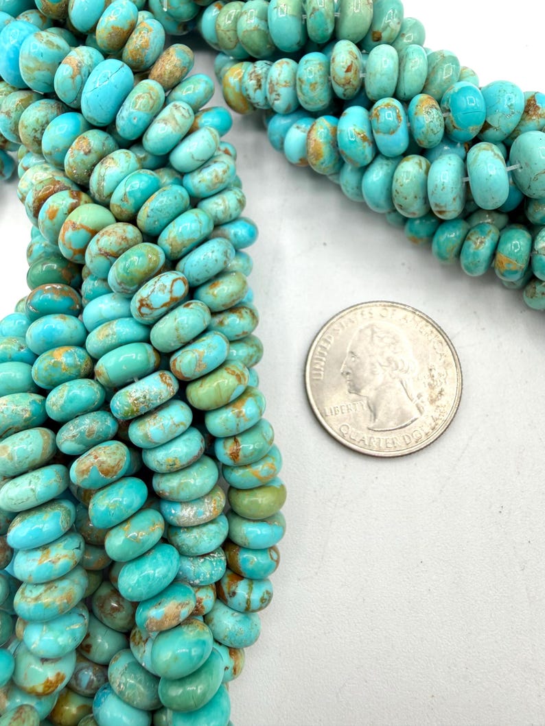 May include: A strand of round, disc-shaped turquoise beads featuring natural brown matrix veining in shades of bright blue and green. A United States quarter coin is placed next to the beads to provide a clear sense of scale for the bead size.
