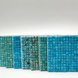 May include: A collection of six rectangular mosaic tiles arranged in a row, each featuring a grid of small square pieces in varying shades of turquoise, teal, and blue, with some tiles displaying natural brown veining and colour variations.