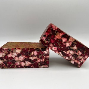 May include: Two rectangular blocks with a mosaic pattern. The blocks feature a mix of burgundy, pink, and cream-colored fragments set in a tan matrix. One block is upright, while the other is leaning against it.