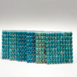 Peut inclure: Cinq cartes de présentation rectangulaires contenant chacune une grille de petits cabochons de turquoise ovales. Les pierres varient dans des tons de bleu et de vert, certaines présentant des motifs de matrice brune, disposées en rangées.
