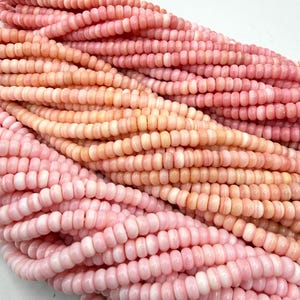 May include: Multiple strands of small, round, disc-shaped beads in varying shades of soft pink and light peach. The beads are arranged in parallel rows, showcasing a smooth, uniform texture and a consistent size across all the individual strands.