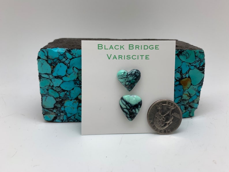 May include: Two heart-shaped turquoise variscite cabochons, one green and one blue, with black veins, on a white card with the text "Black Bridge Variscite". A US quarter is shown for scale.