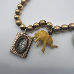 Puede incluir: Un collar de cuentas doradas con un peque&ntilde;o medall&oacute;n de oro y un dije de elefante de marfil tallado.