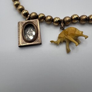 Puede incluir: Un collar de cadena de oro con un peque&ntilde;o medall&oacute;n y un dije de elefante de marfil tallado. El medall&oacute;n tiene una ventana de vidrio y un marco de oro.