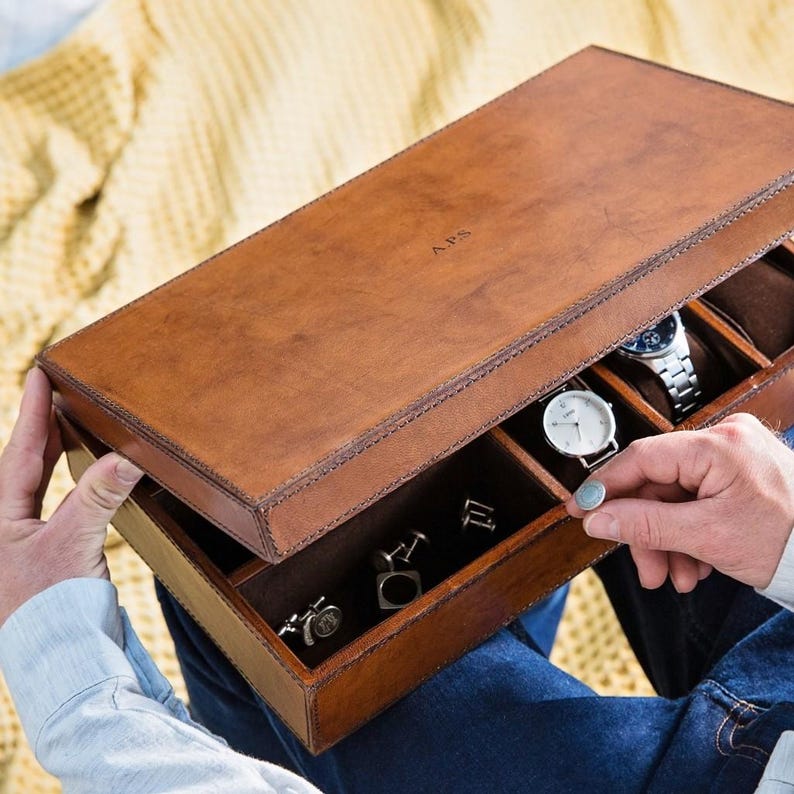 May include: A brown leather watch and jewellery box with a compartment for cufflinks and a section for watches. The box is open and the lid has the initials "A.P.S." engraved on it.