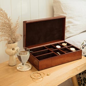 May include: A brown leather watch box with a hinged lid and multiple compartments for storing watches. The box is open and empty, revealing the compartments.