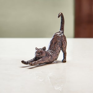 May include: A bronze sculpture of a cat stretching, with its tail curled up and its body arched. The cat is depicted in a realistic style, with detailed fur and facial features.