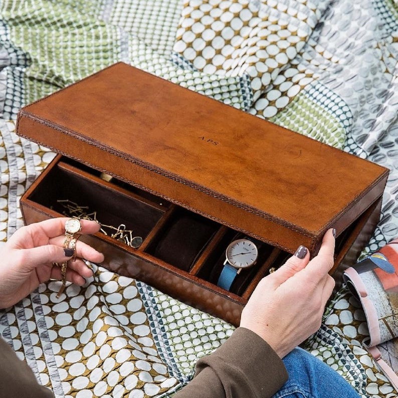 May include: A brown leather box with a hinged lid and compartments for storing jewelry and watches. The box is personalized with the name "Alex".