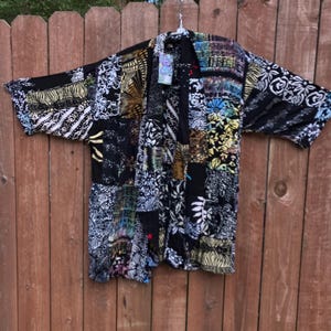 May include: A black and white patterned kimono with a short sleeve. The kimono has a patchwork design with various floral and geometric patterns.