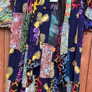 May include: A blue patchwork kimono with a colorful pineapple print. The kimono has a long, flowing silhouette and is made of a lightweight fabric. The fabric is made of a variety of different materials, including silk, cotton, and rayon. The kimono is perfect for layering over a simple outfit or for wearing on its own.