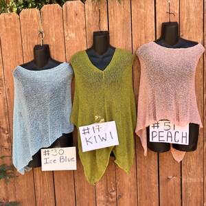 May include: Three lightweight knit ponchos in ice blue, kiwi green, and peach. Each poncho is displayed on a black mannequin. White cards are attached to each, labeled #30 Ice Blue, #17 KIWI, and #51 PEACH, identifying the specific color of each garment.