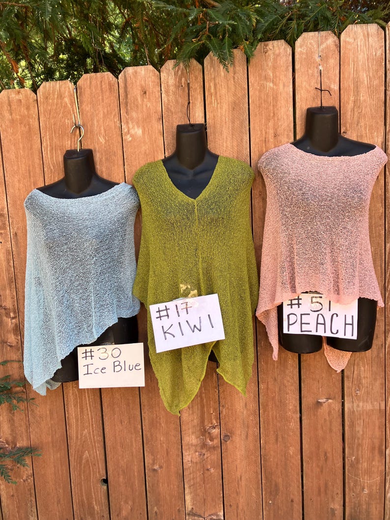 May include: Three lightweight knit ponchos in ice blue, kiwi green, and peach. Each poncho is displayed on a black mannequin. White cards are attached to each, labeled #30 Ice Blue, #17 KIWI, and #51 PEACH, identifying the specific color of each garment.