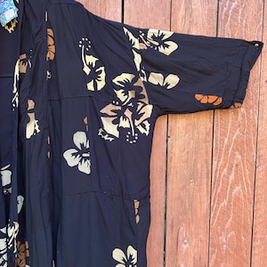 May include: A dark navy blue kimono-style robe with a floral pattern in shades of beige and brown. The robe has long sleeves and a loose, flowing design. The background is a wooden surface.