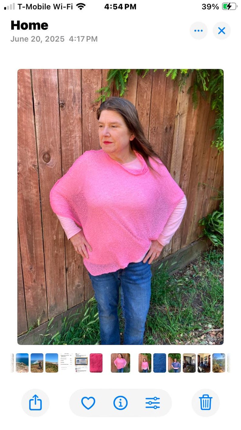 May include: A bright pink, loose-fitting, semi-sheer knit poncho with a wide neckline, worn over a light pink long-sleeved shirt and blue denim jeans. The poncho features a textured, open-weave fabric that drapes over the shoulders and torso.