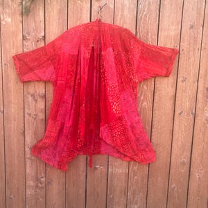 May include: A bright red open-front kimono-style jacket featuring a patchwork design with various tonal red patterns, including leaf motifs and dotted textures. The garment has short sleeves, a loose drape, and a lightweight, semi-sheer appearance.