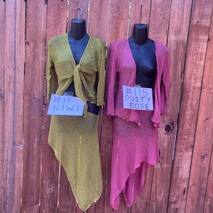 May include: Two long-sleeved, open-front knit tops and matching asymmetrical skirts displayed on mannequins. One set is kiwi green with a tag reading #17 KIWI, and the other is dusty rose with a tag reading #115 DUSTY ROSE. Both feature a textured knit.
