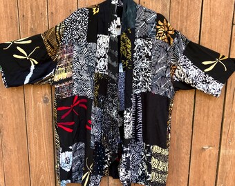 May include: A patchwork kimono-style jacket with a variety of patterns and colors. The jacket features black, white, gold, and red designs, including floral and dragonfly motifs. It hangs on a wooden background.