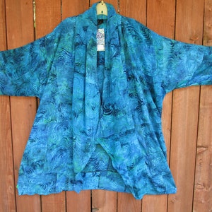 May include: A blue and green patterned kimono-style cardigan with a draped collar. The fabric has a swirling, wave-like design.