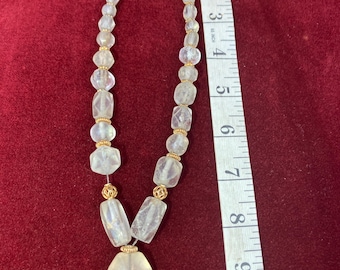 May include: A clear, beaded necklace with gold-colored accents. The necklace features a variety of clear, geometric-shaped beads and a triangular pendant. The necklace is approximately 10 inches long.