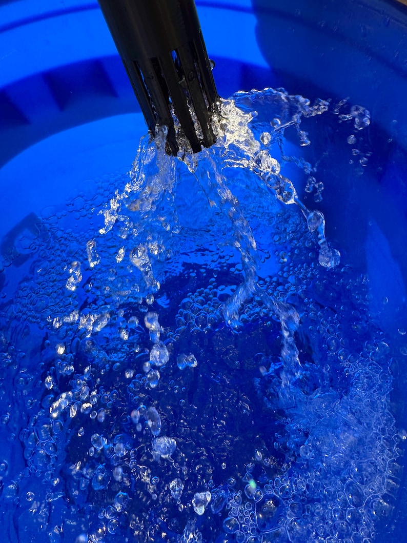 May include: A close-up shot shows water cascading from a black spout into a vibrant blue bucket. The clear water forms droplets and bubbles, contrasting with the blue surface. The image highlights the water's movement and texture.