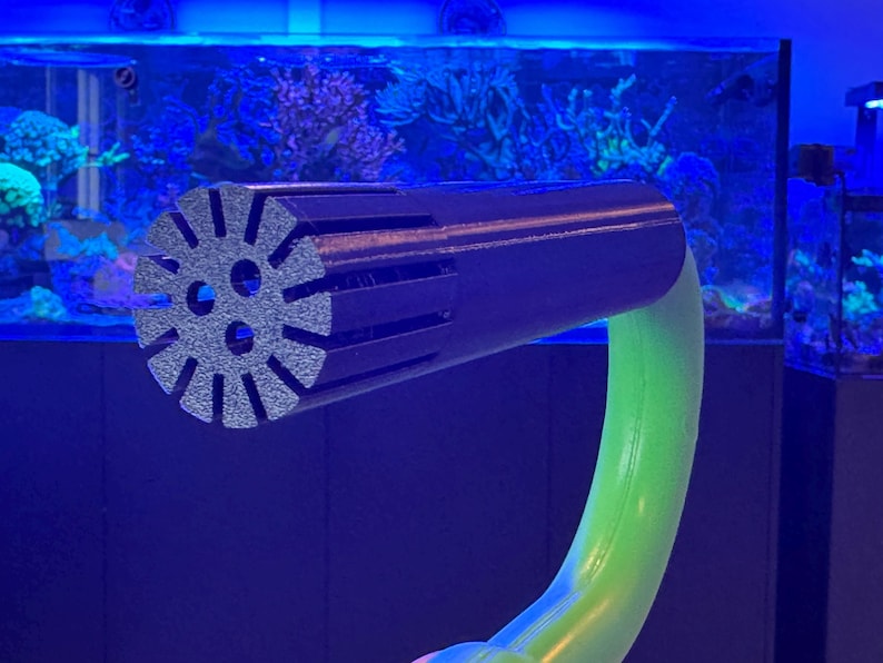 May include: A black and grey aquarium accessory with a circular, slotted head and a curved, green stem. The head has three circular holes and radial slots. The stem is a bright, neon green colour.