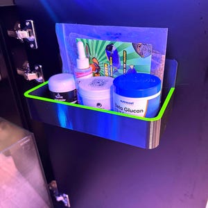 May include: A black and blue shelf with a neon green trim, holding various containers and a bag. The containers include a white jar, a black jar, a bottle with a dropper, and a blue-lidded jar with the text "Beta Glucan". A green and white graphic is visible.