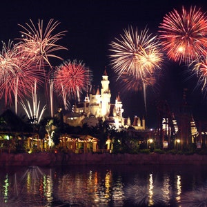 May include: A nighttime view of a castle-like building with fireworks exploding over the water in front of it. The fireworks are red, white, and blue. The text "Universal Studios Singapore" is visible in the bottom right corner of the image.