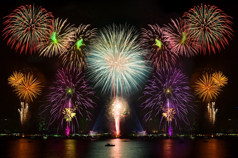 May include: A colorful fireworks display over a body of water. The fireworks are exploding in the night sky, creating a variety of shapes and colors. The water is reflecting the light from the fireworks.
