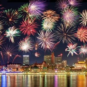 May include: A nighttime cityscape with a vibrant fireworks display. The sky is filled with bursts of red, green, yellow, and purple fireworks. The city skyline is illuminated with lights reflecting on the water below.