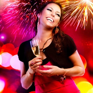 May include: A woman in a red dress and black bolero jacket holds a champagne flute, smiling against a backdrop of fireworks and bokeh lights. She wears jewelry, including earrings, a necklace, and a bracelet.