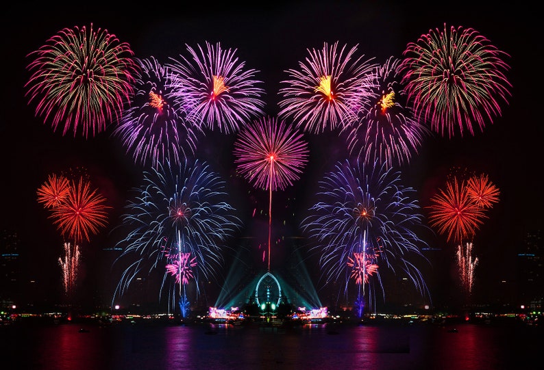 May include: A night sky filled with colorful fireworks exploding over a city skyline. The fireworks are a mix of red, pink, blue, and white.