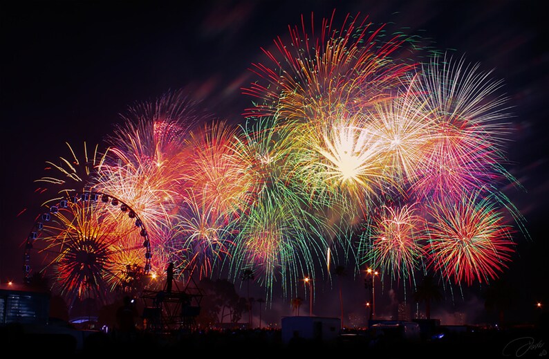 May include: A colorful fireworks display explodes in the night sky over a Ferris wheel. The fireworks are red, orange, yellow, green, and blue.