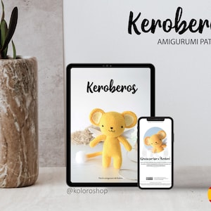 May include: A digital tablet and a smartphone display a crochet pattern for a yellow amigurumi toy named Keroberos. The pattern includes instructions for making the toy and a picture of the finished product. The text on the screen reads "Keroberos Amigurumi Pattern".