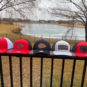 May include: Four different baseball caps with a black mesh back and a variety of coloured fronts. The caps feature a brown leather patch with the words "Chiefs Kingdom" and a stylised arrowhead design.