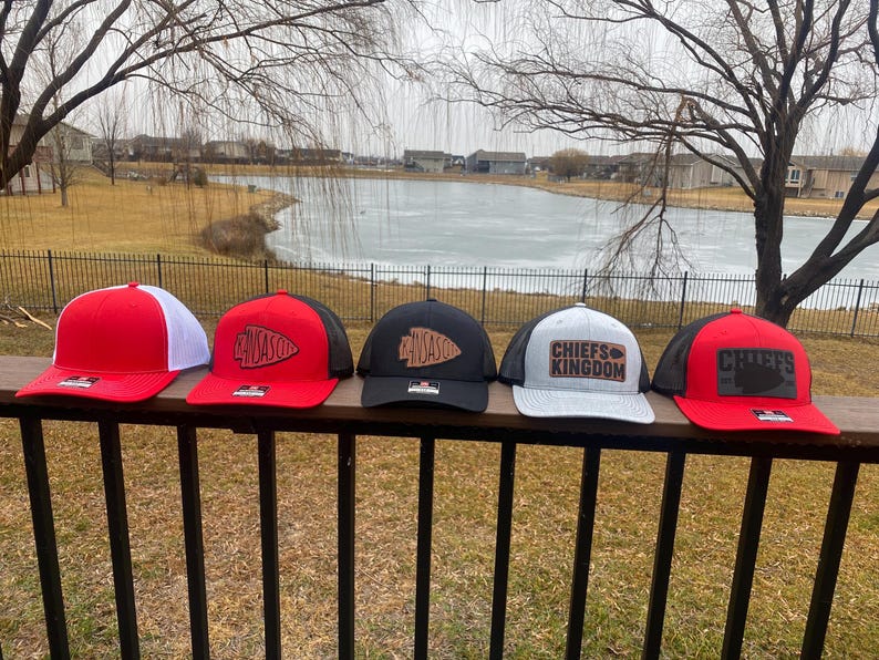 May include: Four different baseball caps with a black mesh back and a variety of coloured fronts. The caps feature a brown leather patch with the words "Chiefs Kingdom" and a stylised arrowhead design.