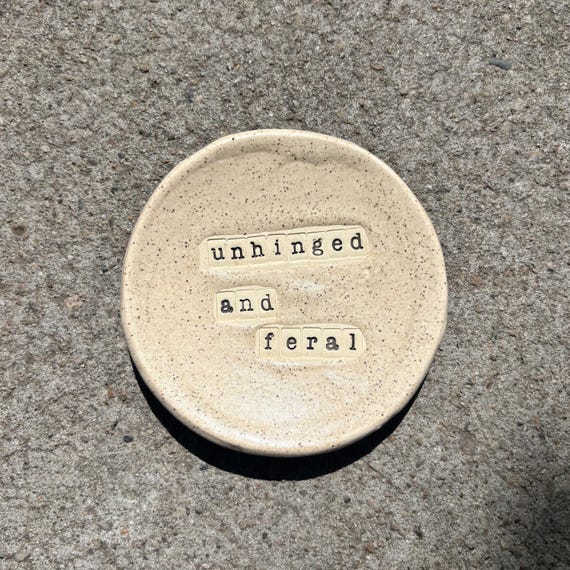 A handmade stoneware ring dish stamped with "Unhinged & Feral" — sturdy, real ceramic (not air-dry clay), and speaks directly to a very specific, very relatable energy.