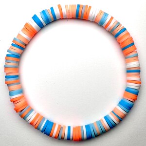 May include: A colorful bracelet made of stacked, round beads in shades of peach, white, and blue.