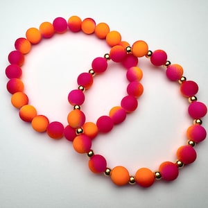 May include: Two bracelets with pink and orange ombre beads and gold accents.