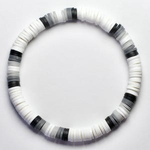 May include: A circular bracelet composed of small, flat, disc-shaped beads. The beads alternate between white, black, and shades of gray, creating a monochromatic pattern. The bracelet is designed to be worn around the wrist.