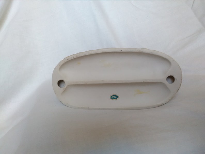 Może przedstawiać: Sp&oacute;d białej ceramicznej figurki z zieloną naklejką z napisem "Made in Japan".