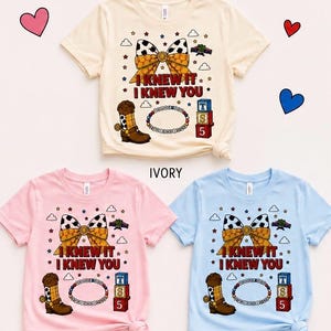 Pu&ograve; includere: Tre magliette a maniche corte in avorio, rosa fiore e blu chambray. Ogni maglietta presenta una grafica con un fiocco a stampa mucca, uno stivale da cowboy marrone, un braccialetto di perline, blocchi alfabetici e il testo I KNEW IT I KNEW YOU.