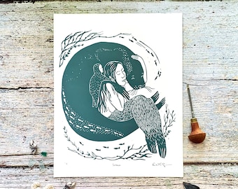 May include: A teal and white linocut print titled "Selkie" depicts a woman embracing a seal within a circular design. The artwork features detailed linework, with fish and aquatic plants. The artist's signature is visible.