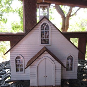 May include: A white wooden model of a church with a brown roof, stained glass windows, and a small steeple. The church is sitting on a black and white patterned table.