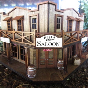 May include: A wooden model of a saloon building with a sign that reads "Bella Union Saloon" and "Craps". The building has a balcony and two barrels in front of it.