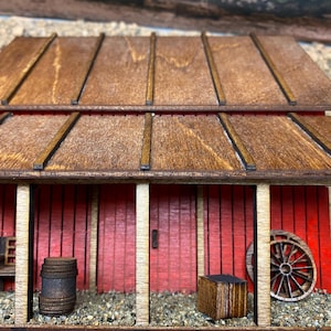 May include: A miniature wooden barn with a red exterior and a brown wooden roof. The barn features a small porch with a bench, a barrel, and a wagon wheel. The roof has a slatted design.
