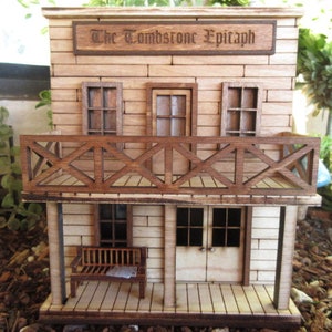 May include: A wooden model of a two-story building with a balcony and a sign that reads "The Tombstone Epitaph". The building is painted in a light brown color and has a wooden door and windows.